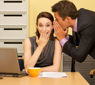 Businessman whispering in businesswoman's ear at office