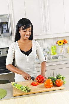 Smiling black woman cutting vegetables in modern kitchen interior