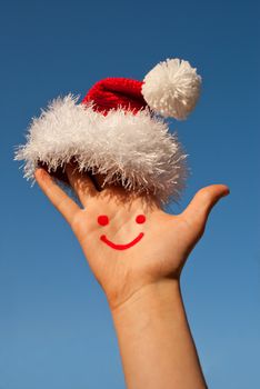 Human's palm with smile on it wearing Santa's hat