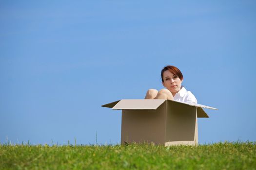 Young woman sitting in cardboard box at park
