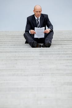 Businessman reading document on steps
