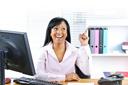 Smiling black business woman pointing up with idea at desk in office