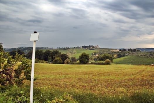 Pole with blank sign overlooking Tuscan hills with dramatic sky