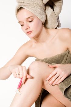 Young woman in towel on a white background shaving