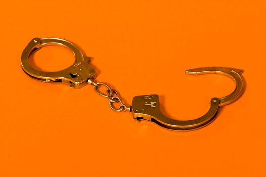 Open metal handcuffs on the orange background