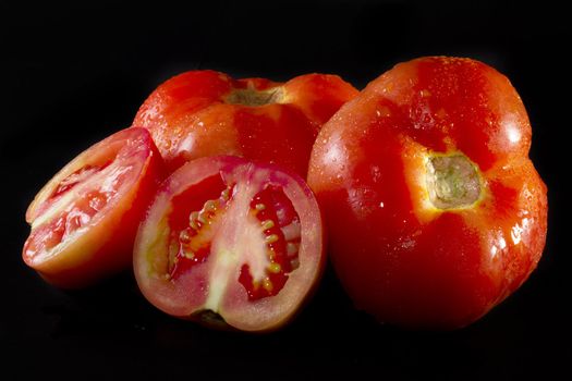 Close up view of a bunch of red tomatoes isolated on a black background. 