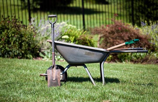 Spade resting against a wheelbarrow in a flower filled back garden