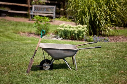 Spade resting against a wheelbarrow in a flower filled back garden with seat in background