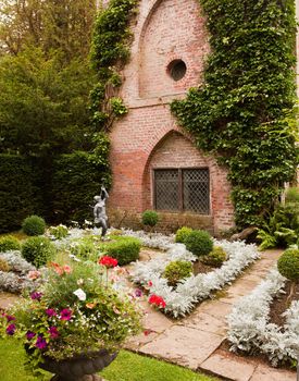 Formal flower beds in front of old brick building with statue