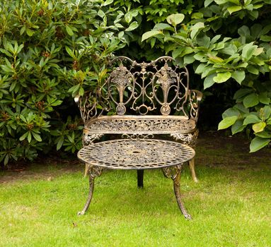 Old fashioned gold colored cast iron table and bench on formal lawn