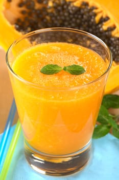 Fresh blended papaya juice with a mint leaf as garnish on top and a papaya half in the back (Selective Focus, Focus on the mint leaf) 