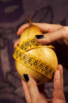 View of a woman's hand grabbing a pear with measuring tape.