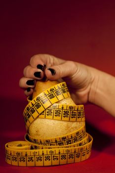 View of a woman's hand grabbing a pear with measuring tape.