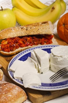 View of a dish of fresh cheese with sandwich of chorizo and fruit.