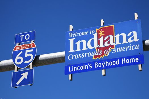 Welcome to Indiana and highway65 road sign against blue sky.