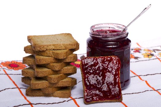 Close view of a toasted bread with berry jam jar isolated on a white background.