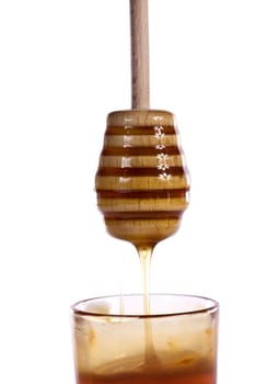 Close up view of a glass of honey with dipper isolated on a white background.