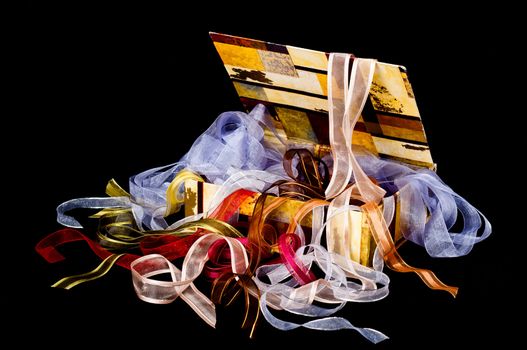 Beautiful box overflowing with colorful ribbons on a black background