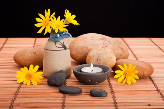 Spa still life with pebbles, candle and yellow daisies on bamboo mat