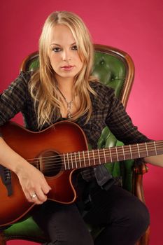 Photo of a female guitarist playing while sitting on a green leather chair.