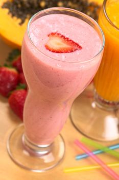 Strawberry milkshake with a strawberry slice on top and papaya juice behind (Selective Focus, Focus on the front edge of the strawberry slice) 