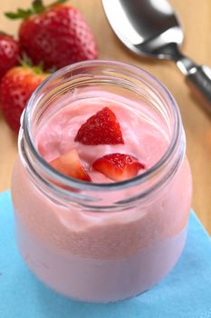 Strawberry yogurt in glass with fresh strawberry pieces (Selective Focus, Focus on the strawberry piece further away)  