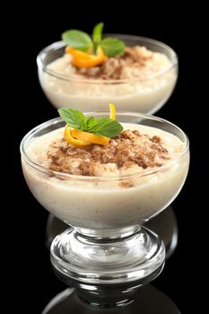 Delicious homemade rice pudding with cinnamon garnished with orange peel and mint leaf photographed on black (Selective Focus, Focus on the orange peel and the mint leaf on the first dessert)