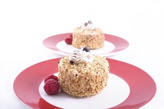 Two hazelnut cakes on red plates garnished with raspberries.  Isolated on white.