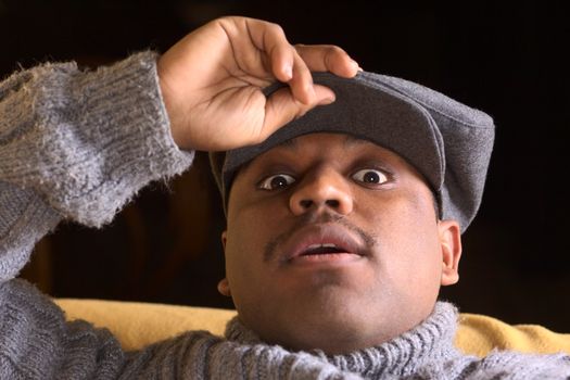 Portrait of a startled young man of African descent with a cap lying on a sofa (Selective Focus, Focus on the eyes)