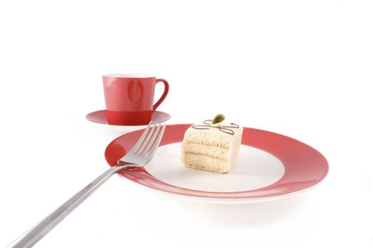 Petit four on red and white plate with fork and red coffee cup.  Isolated on white.