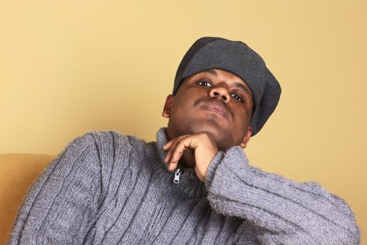 Portrait of a young man of African descent with a cap sitting on a sofa (Selective Focus, Focus on the eyes)