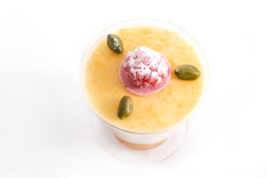 Cup of mango vanilla mousse with raspberry and pistachio topping.  Shot from above with white background.