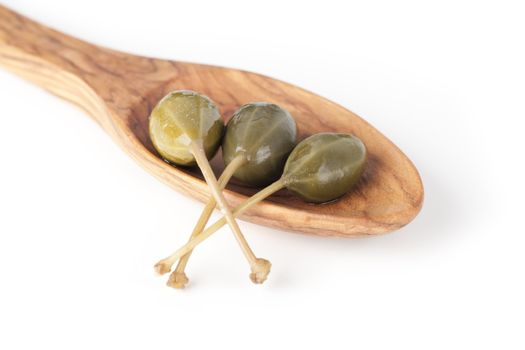 Three large capers in a wooden spoon isolated on a white background.