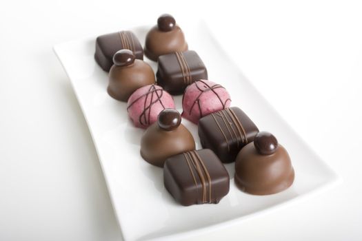 Variety of gourmet chocolates on long glass platter with white background.