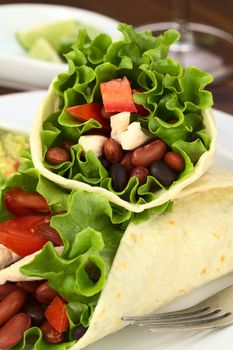 Mexican tortilla wraps filled with chicken, beans, tomato and lettuce (Selective Focus, Focus on the stuffing of the upper wrap)