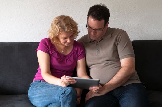 Middle-aged couple sitting comfortably on a sofa and checking a digital tablet pc