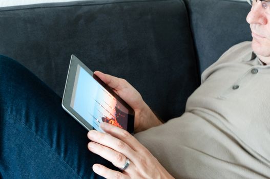 Middle-aged man sitting comfortably on a sofa and checking a digital tablet pc