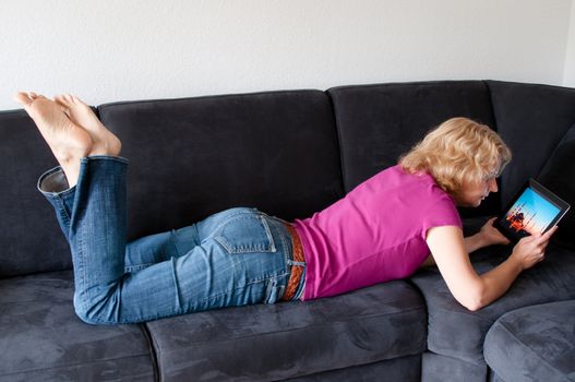 Middle-aged woman laying comfortably on a sofa and checking a digital tablet pc