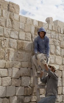 Goreme, Turkey - June 2011: Two Turkish builders up ladders on construction site passing random size stone blocks building dwelling