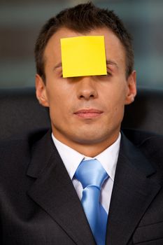 Businessman in office with blank adhesive note stuck to forehead
