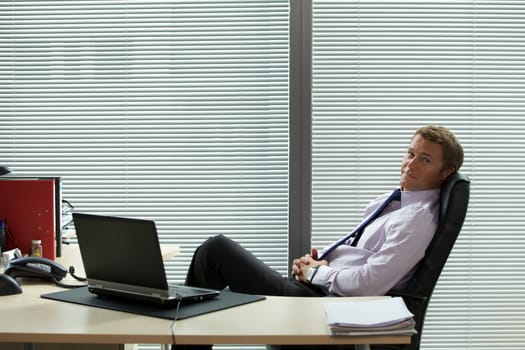 Portrait of businessman relaxing on chair with laptop on desk