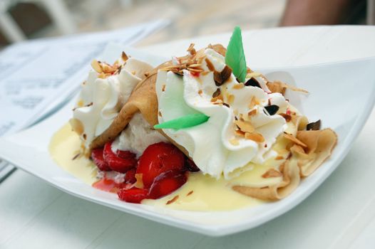 Shot of crepes with ice cream and strawberries in vanilla sauce