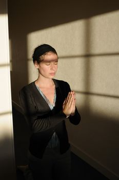 young woman with closed eyes praying in little church