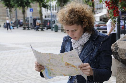 Young curly woman looking at city map, searching for the right way.