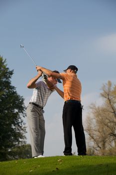 Golf professional helping young man with his swing