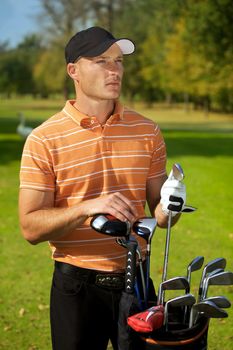 Young man standing by golf bag full of sticks
