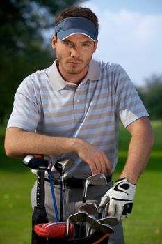 Portrait of young man standing by golf bag full of sticks
