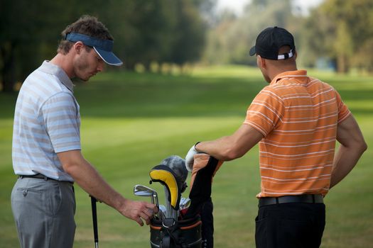 Young men standing in golf course by golf bag full of sticks