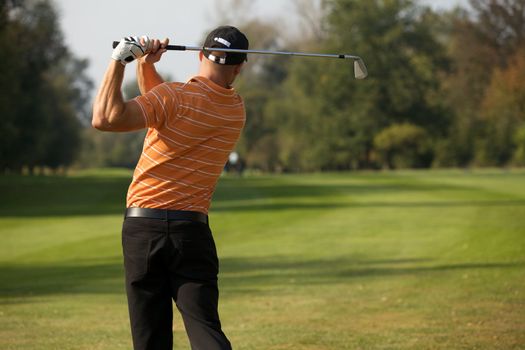 Young man swinging golf club, rear view