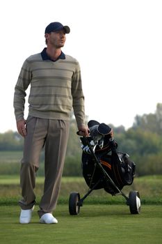 Portrait of young man carrying trolley with golf bag